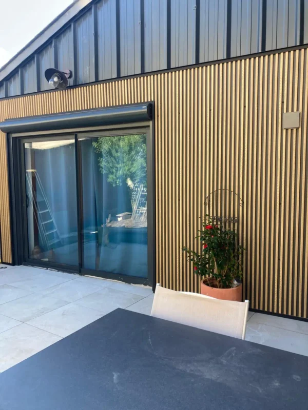 Rénovation de façade avec bardage bois vertical, terrasse en carrelage grès cérame et baie vitrée anthracite, Garcia Rénovation Angers.
