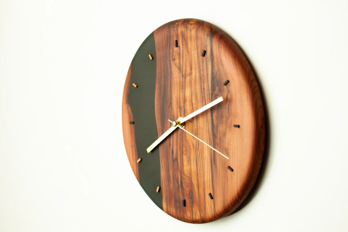 Horloge murale artisanale ronde en bois massif et résine époxy noire avec aiguilles dorées, création Garcia Collection.