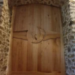 Porte intérieure monumentale en bois massif avec motifs sculptés en relief (lune et colibri), encadrée par un mur en pierre naturelle, création Garcia Rénovation Angers.