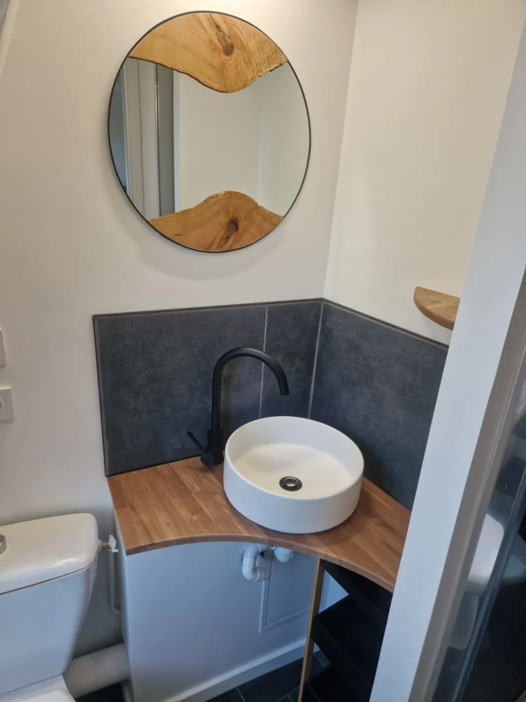 Rénovation salle de bain moderne avec vasque à poser blanche, plan de travail bois sur mesure et miroir organique, Garcia Rénovation Angers.