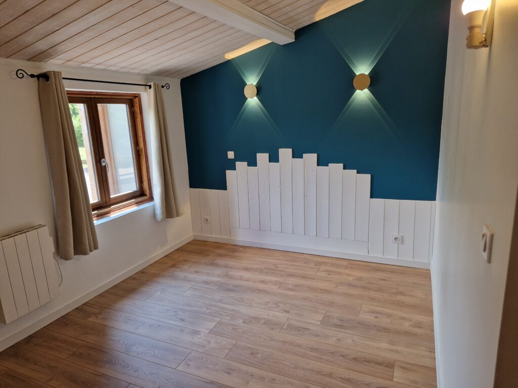 Chambre rénovée avec mur bleu canard, soubassement en lambris blanc découpé et appliques murales