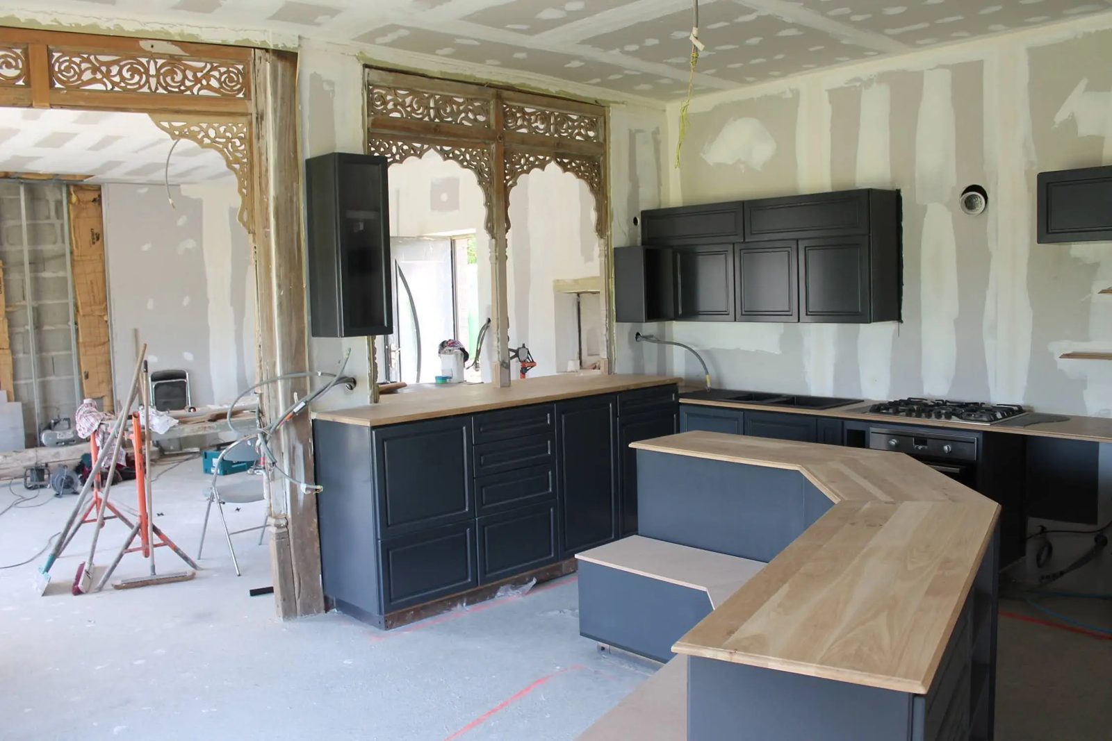 Cuisine aux façades noires avec îlot et plan de travail en chêne massif en cours de pose, boiseries sculptées, près d’Angers