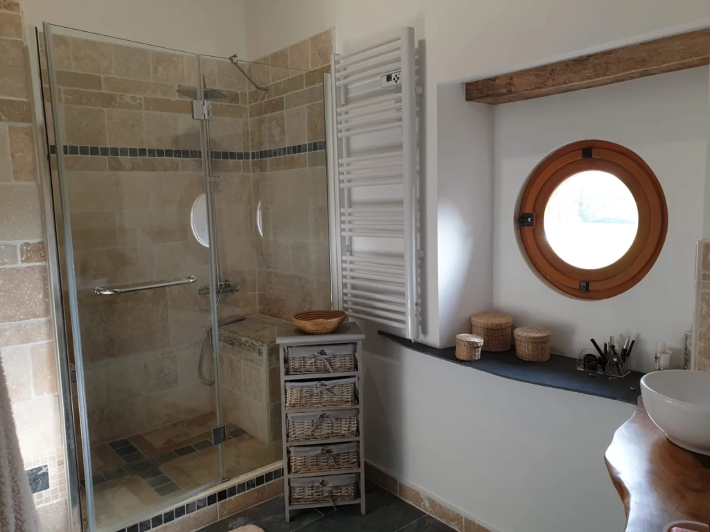 Salle de bain rénovée avec douche vitrée, faïence beige et hublot, par Garcia Rénovation (49)